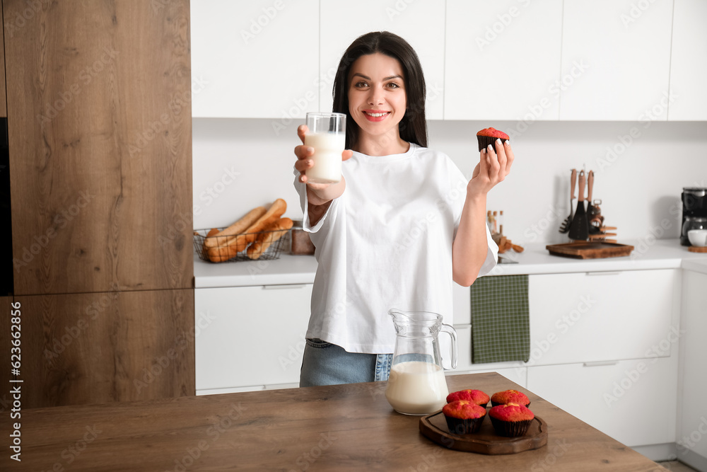 Beautiful woman with tasty muffin and glass of milk in kitchen