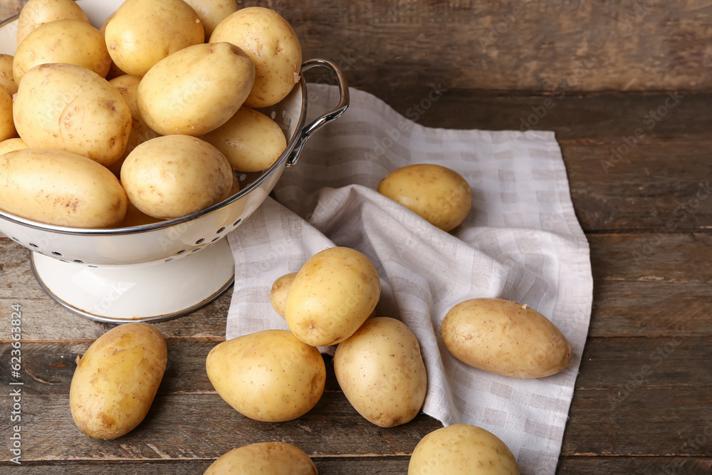 Colander with raw potatoes on wooden background