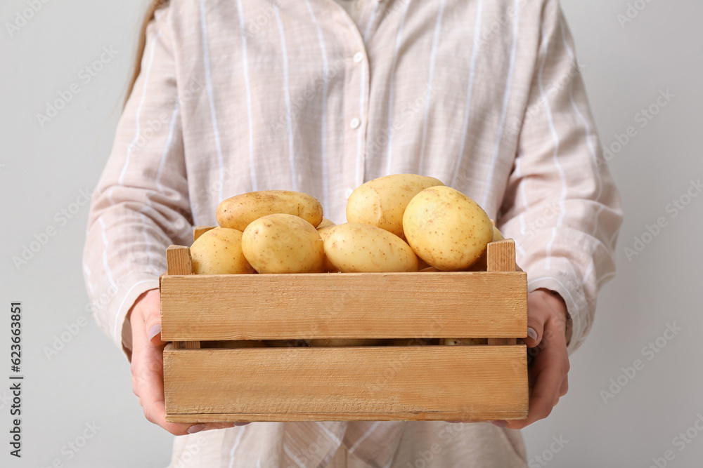 Woman holding wooden box with raw potatoes on light background