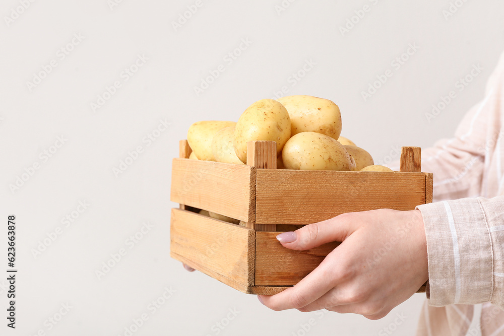 Woman holding wooden box with raw potatoes on light background