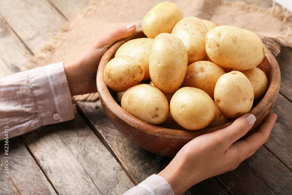 Woman holding bowl with raw potatoes on wooden background