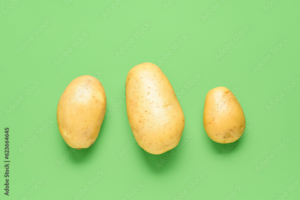 Raw potatoes on green background