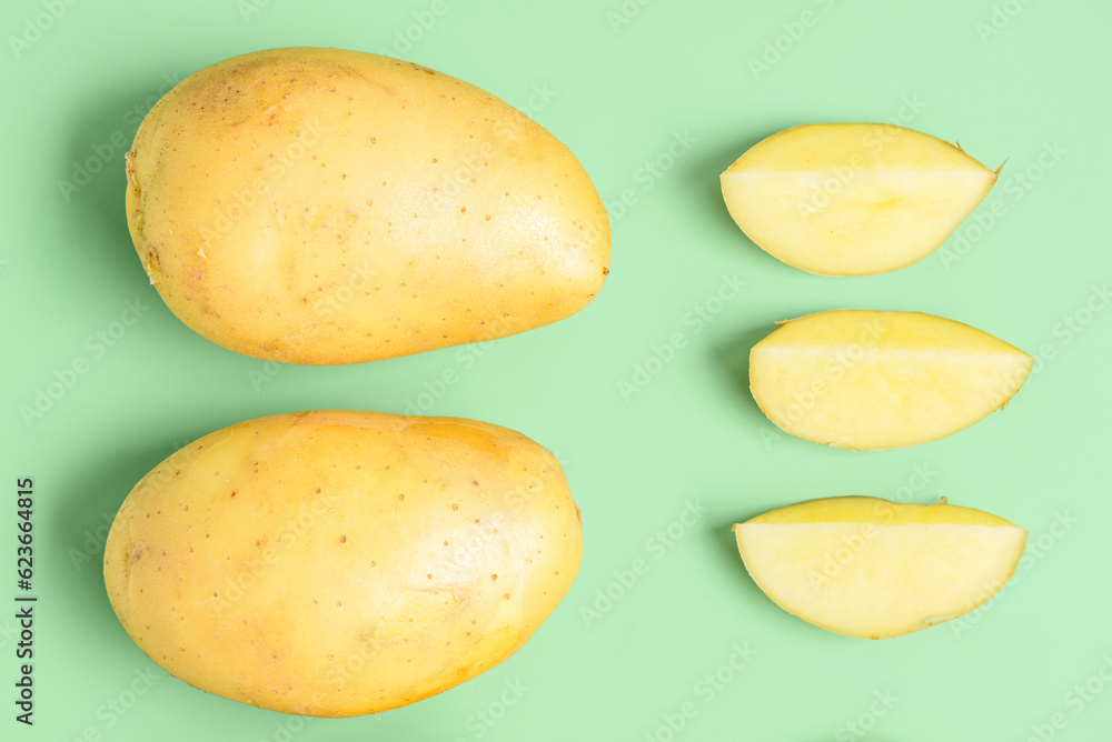 Whole and cut potatoes on green background