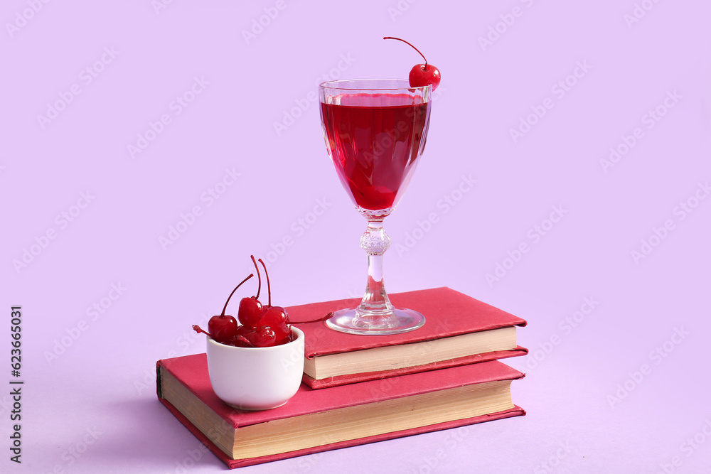 Bowl of tasty maraschino cherries and glass with cold cocktail on lilac background