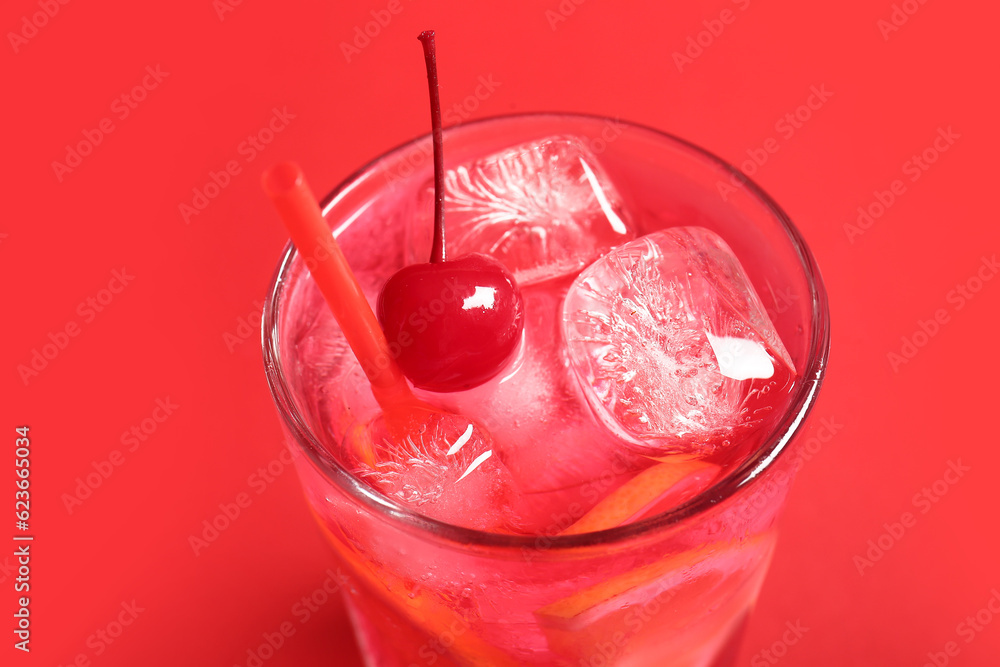 Glass of tasty cocktail with maraschino cherry on red background