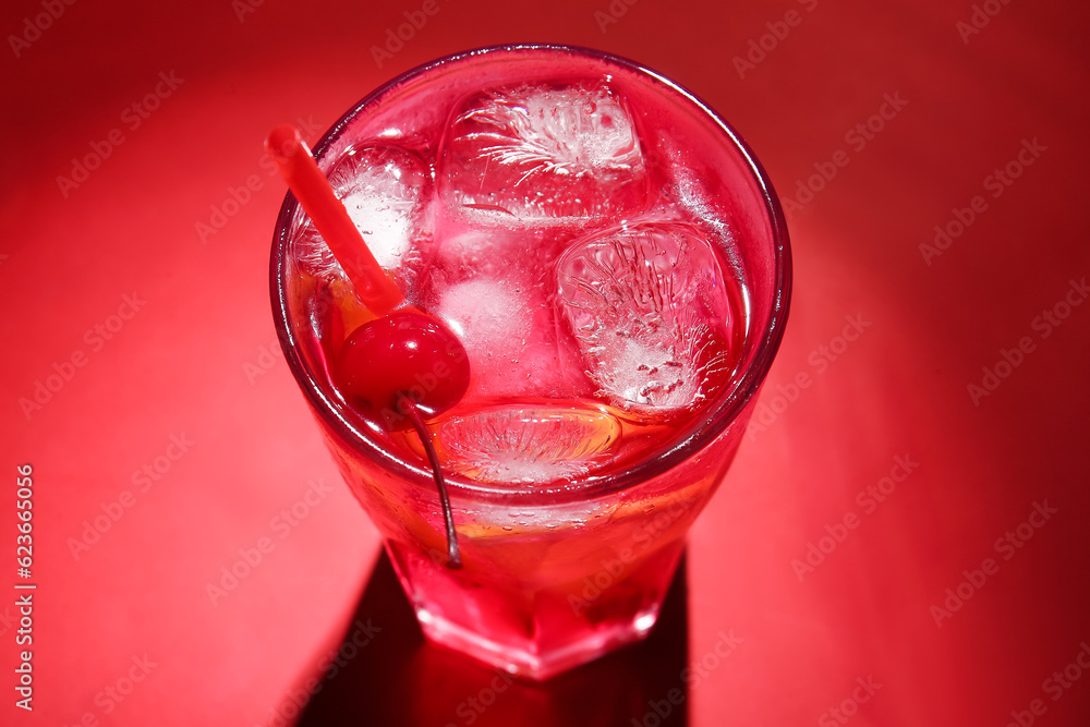 Glass of tasty cocktail with maraschino cherry on red background