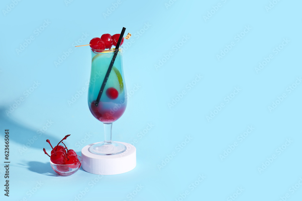 Bowl of tasty maraschino cherries and glass with cold cocktail on blue background