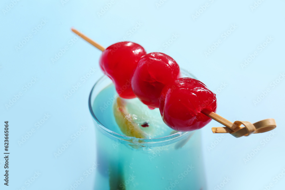 Glass of tasty cocktail with maraschino cherries on blue background