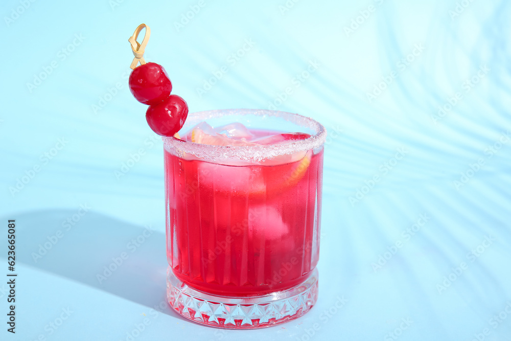 Glass of tasty cocktail with maraschino cherries on blue background