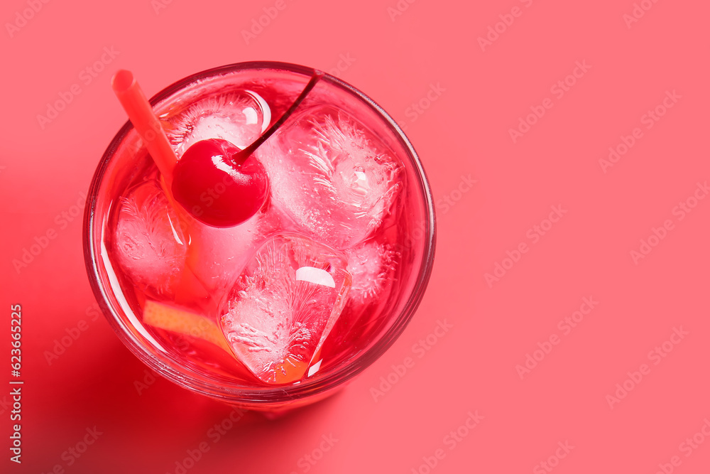 Glass of tasty cocktail with maraschino cherry on red background