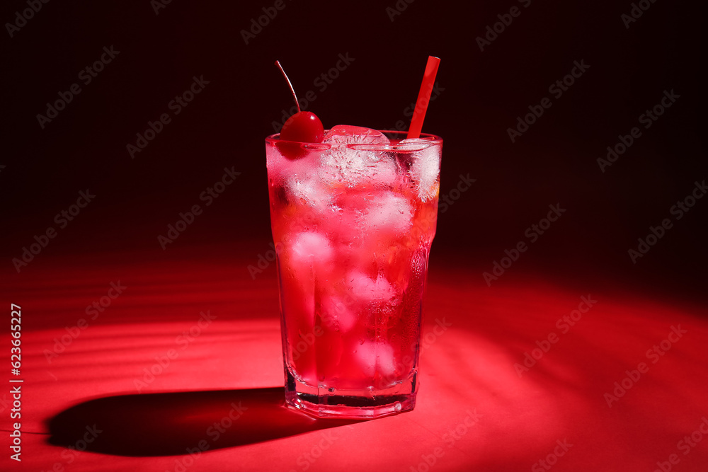 Glass of tasty cocktail with maraschino cherry on red background