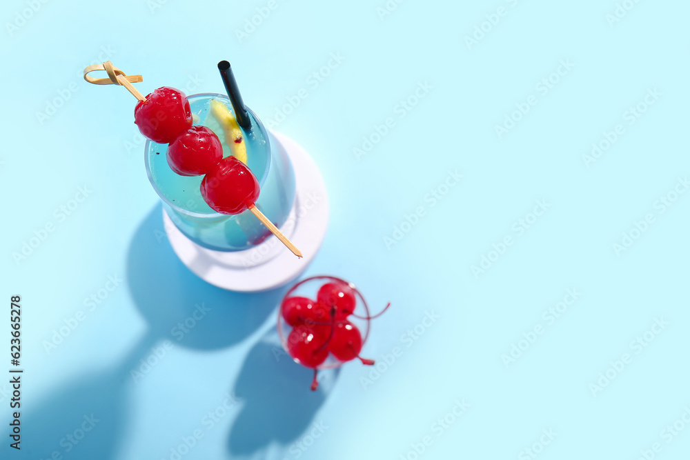 Glass of tasty cocktail with maraschino cherries on blue background