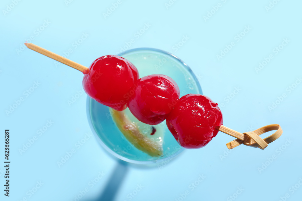 Glass of tasty cocktail with maraschino cherries on blue background