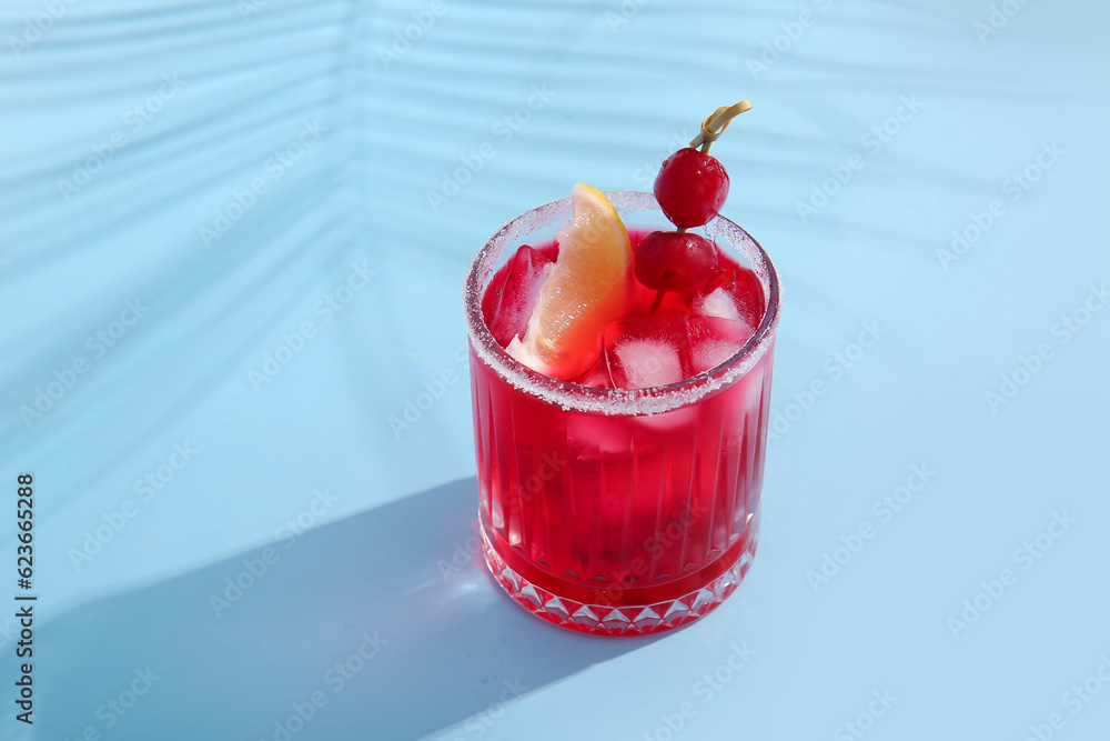 Glass of tasty cocktail with maraschino cherries on blue background