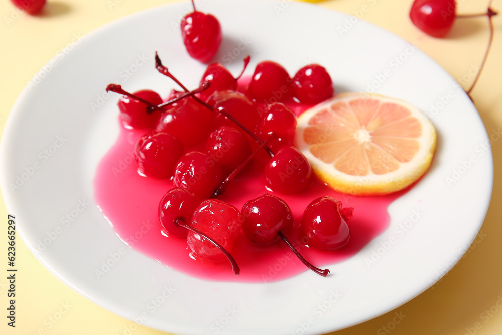 Plate of tasty maraschino cherries and lemon on yellow background