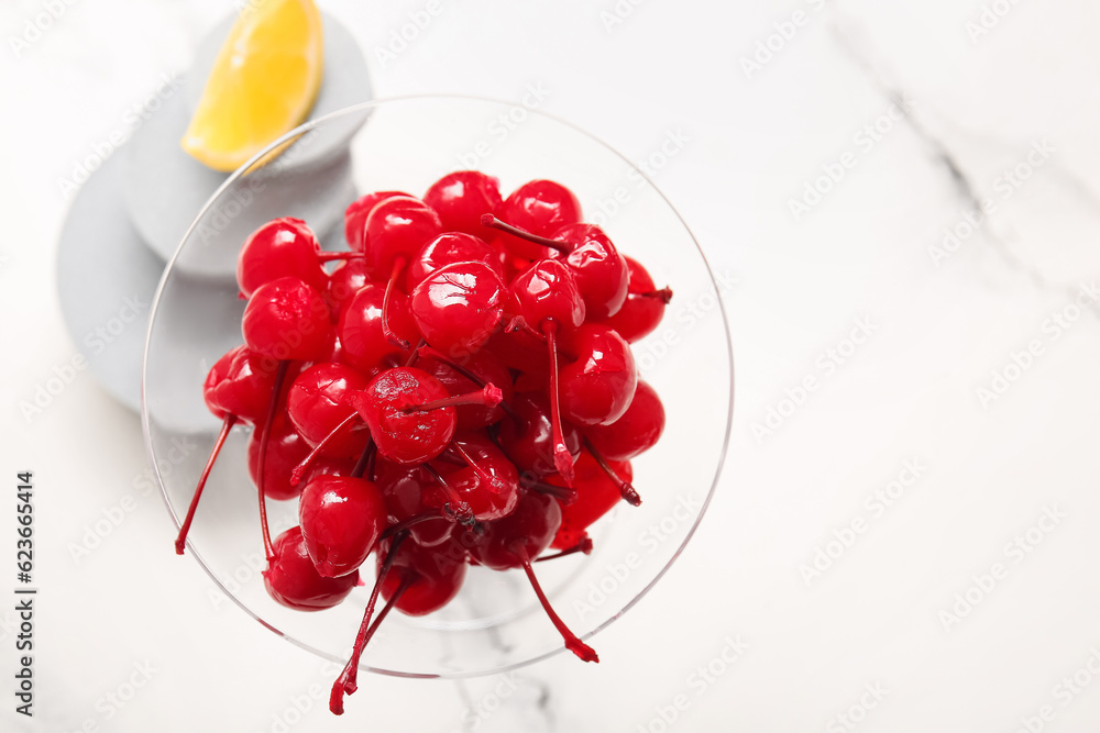 Glass of tasty maraschino cherries on white marble background