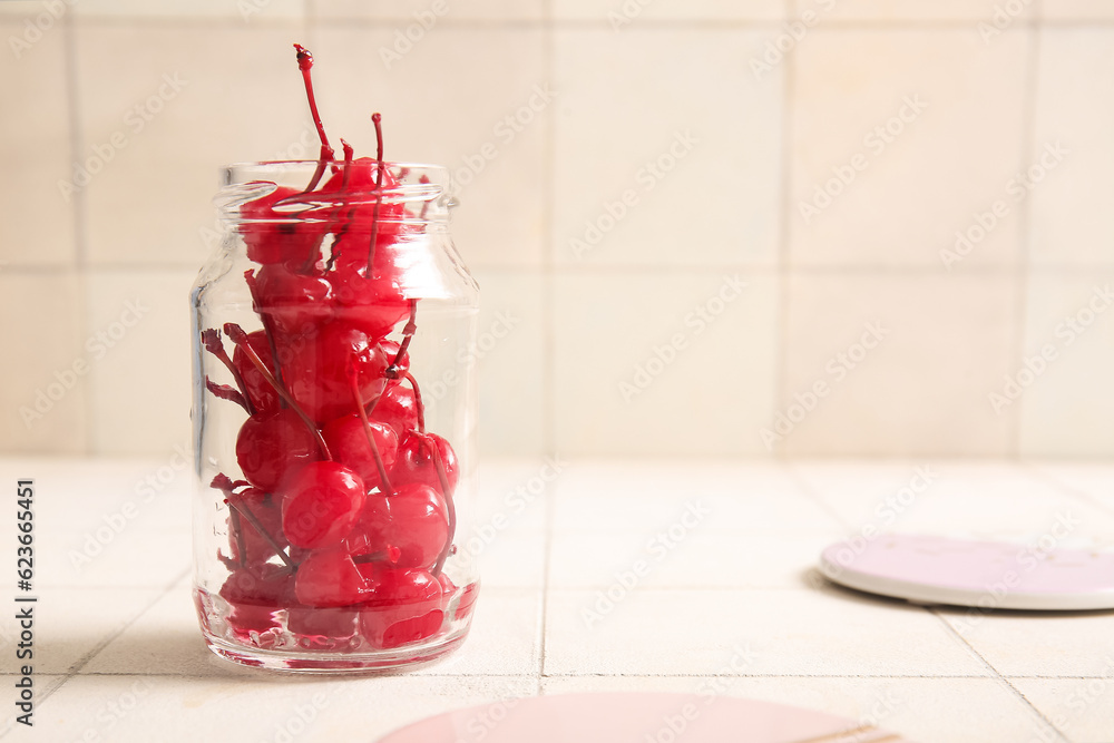 Jar with tasty maraschino cherries on white tile background