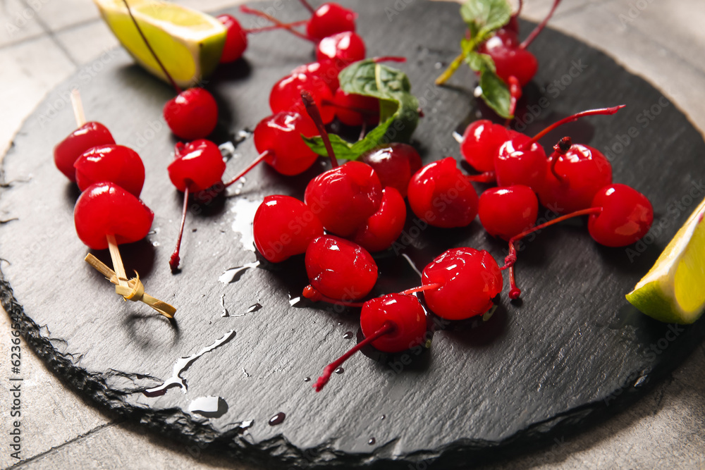 Slate board with tasty maraschino cherries on grey tile background