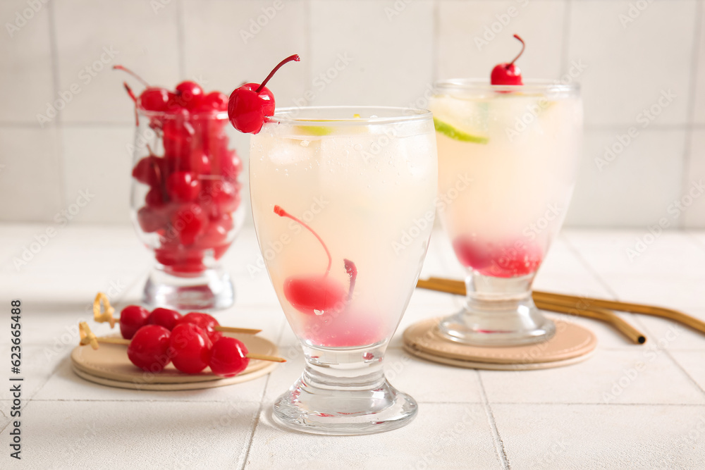 Glasses of tasty cocktail with maraschino cherries on white tile background