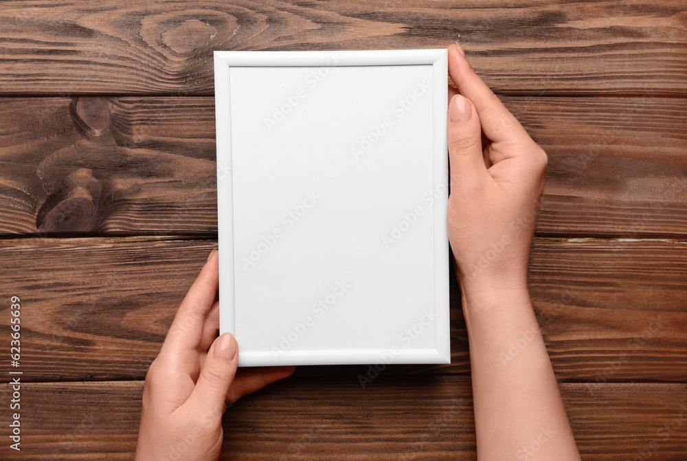 Woman holding blank photo frame on wooden background