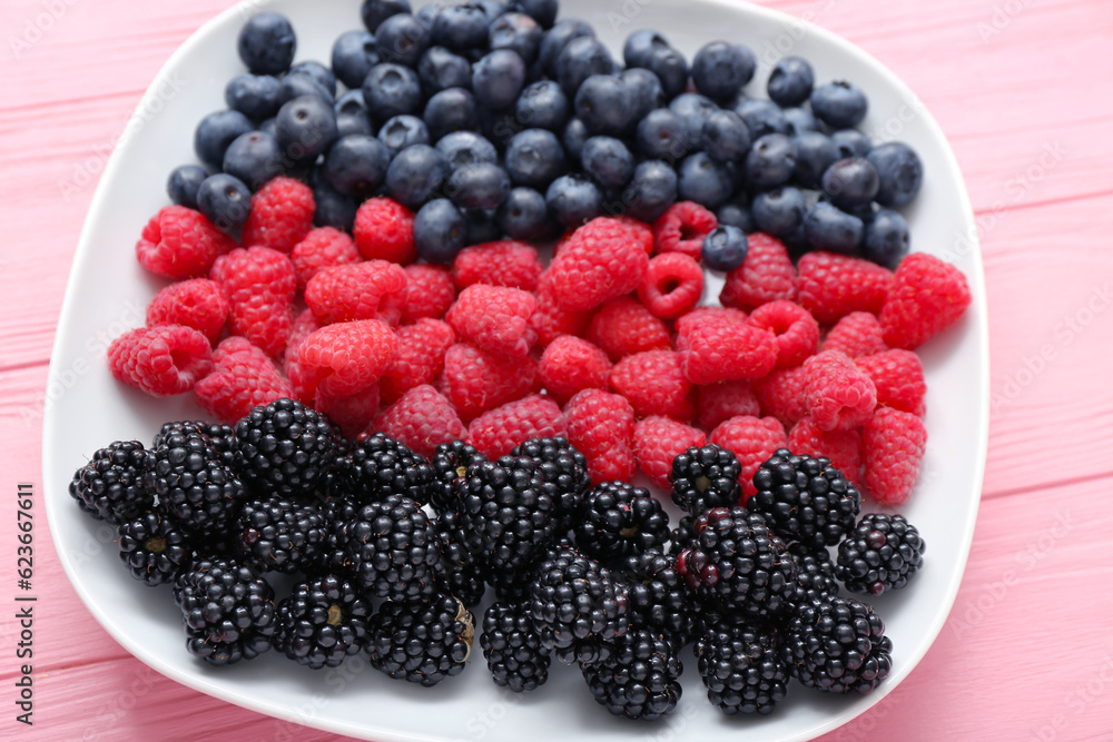 Plate with fresh raspberry, blueberry and blackberry on pink wooden background, closeup