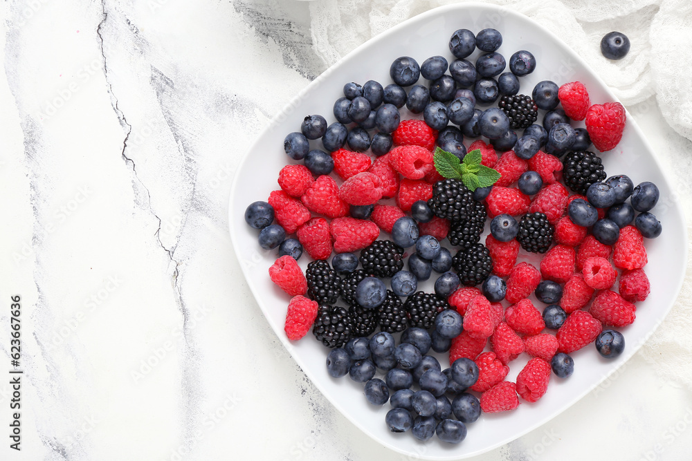 Plate with fresh berries on light background