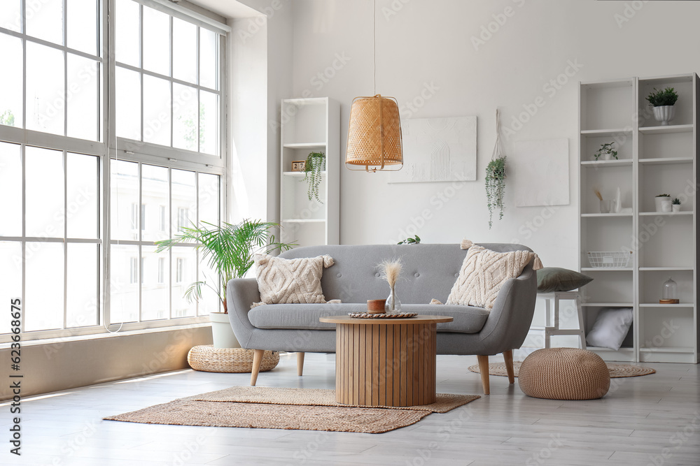 Interior of light living room with grey sofa, wooden coffee table and big window