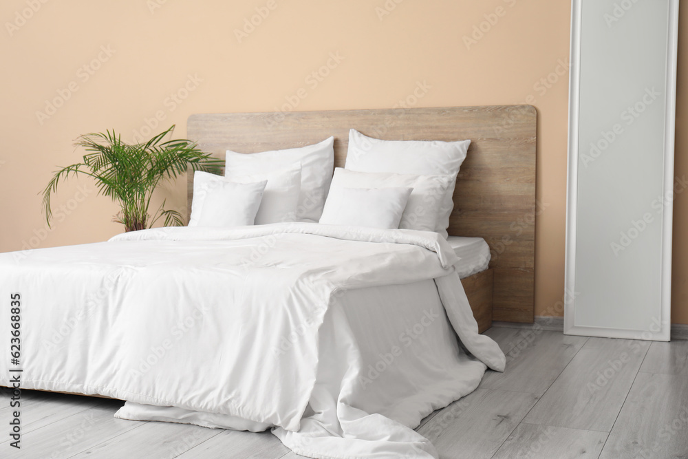 Comfortable bed with white pillows, mirror and houseplant in bedroom