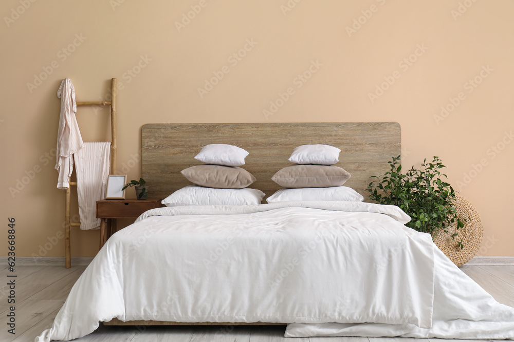 Comfortable bed with white pillows, bedside table and houseplant in bedroom