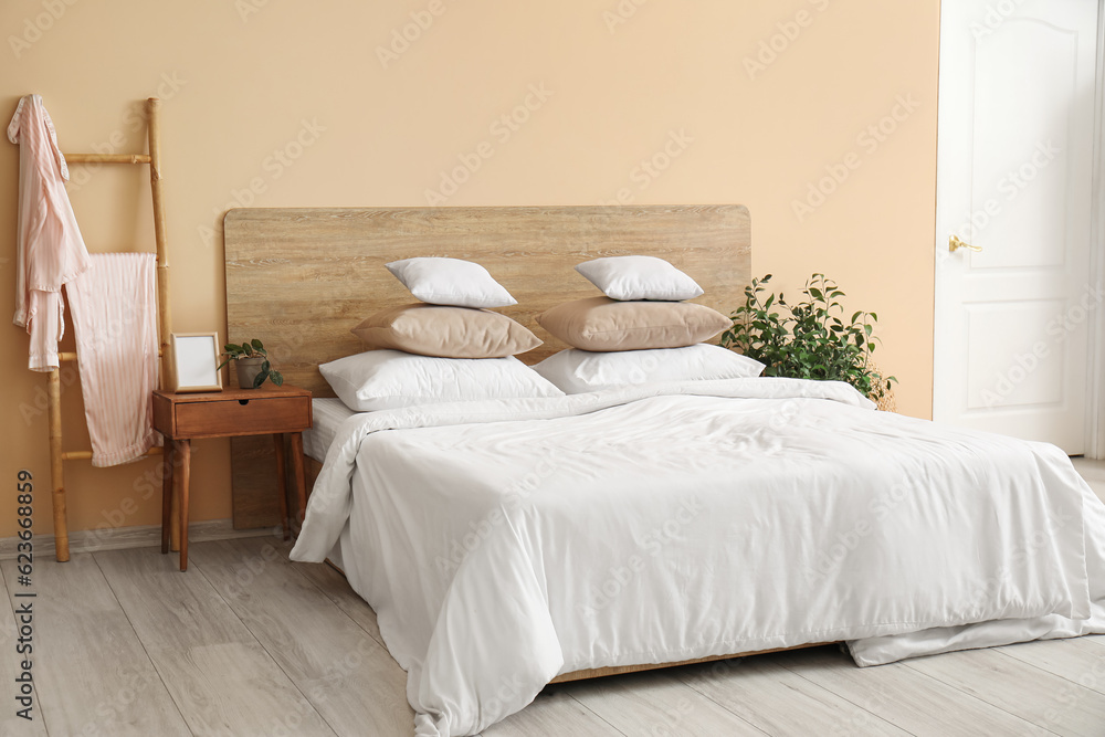 Comfortable bed with white pillows, bedside table and houseplant in bedroom