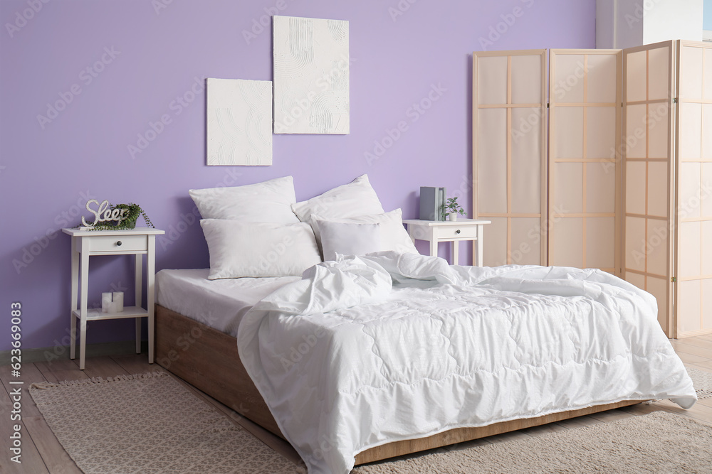 Interior of stylish bedroom with comfortable bed, white pillows, bedside tables and folding screen