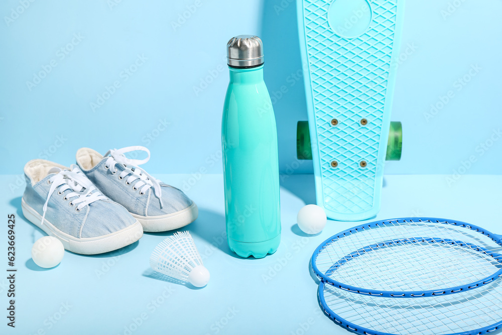 Bottle of water, sports equipment and shoes on color background