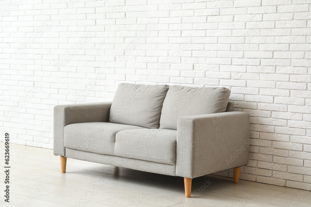 Cozy grey sofa near white brick wall