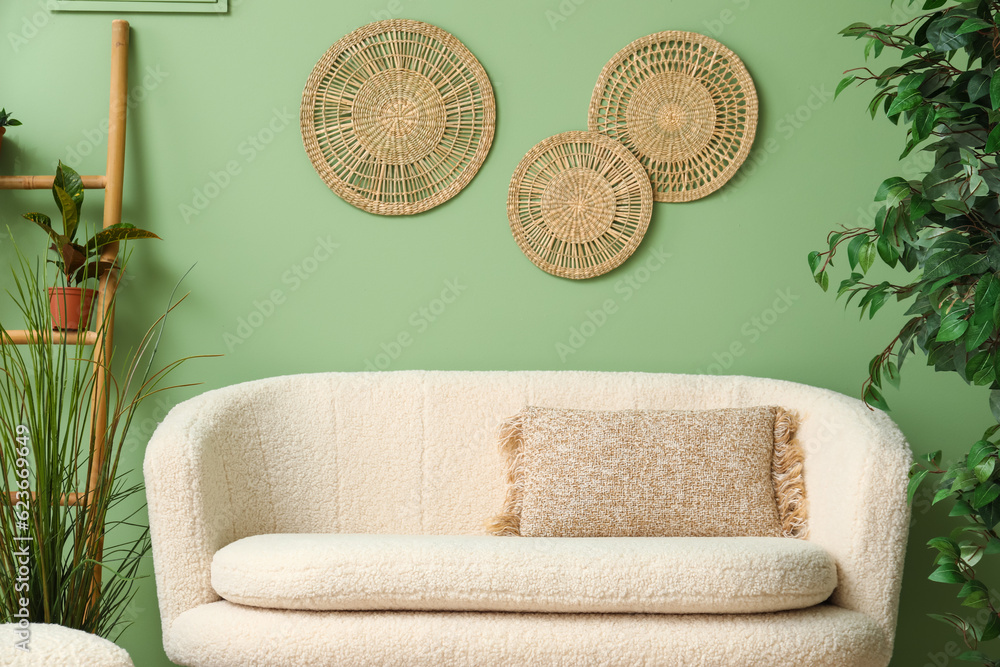 Cozy white sofa with pillow and plants near green wall