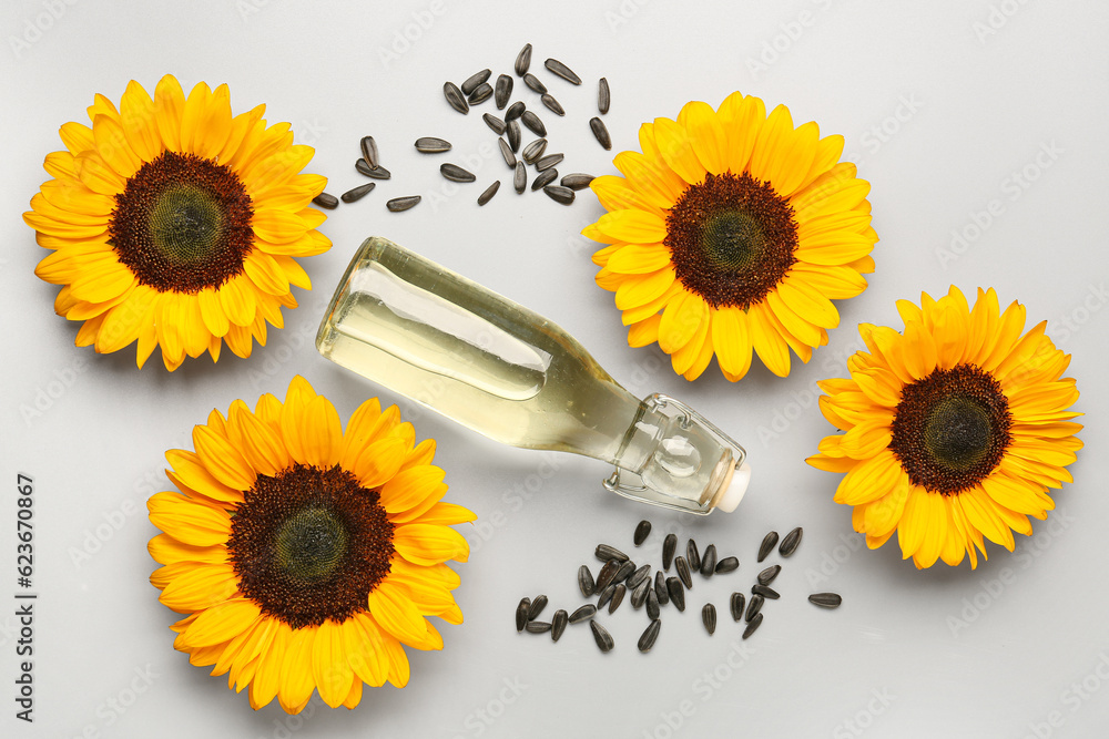 Bottle of oil, sunflowers and seeds on grey background