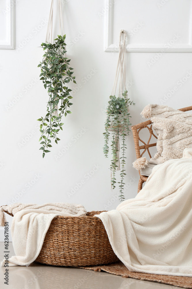 Rattan armchair and wicker basket with cushion near white wall