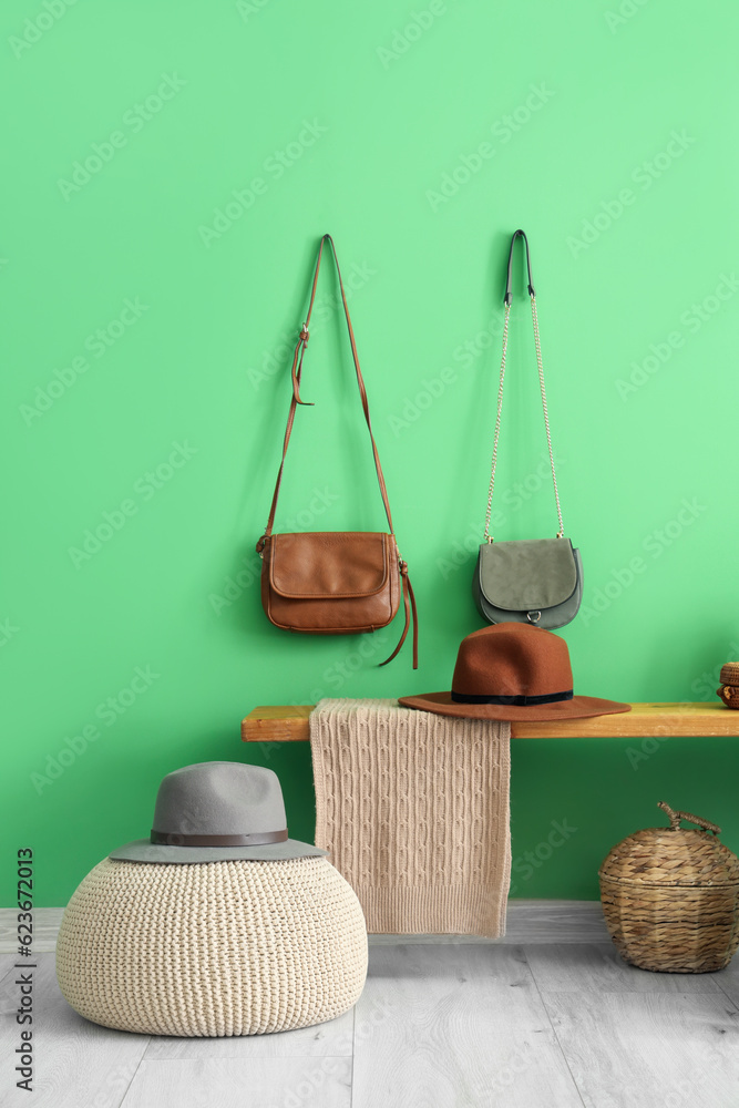 Wooden bench with wicker basket, hats and purses near green wall