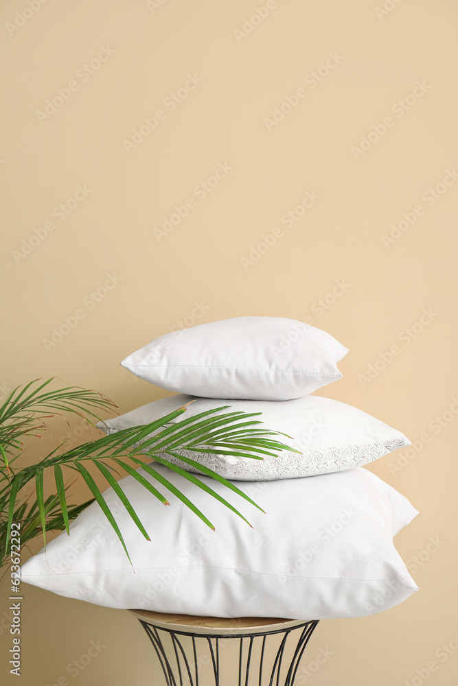 Table with white pillows and houseplant near beige wall