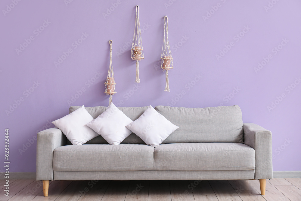 Grey sofa with white pillows near lilac wall