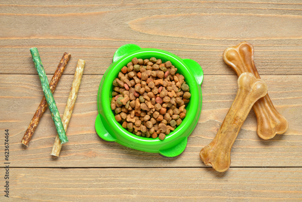 Bowl of dry dog food and treats on wooden background