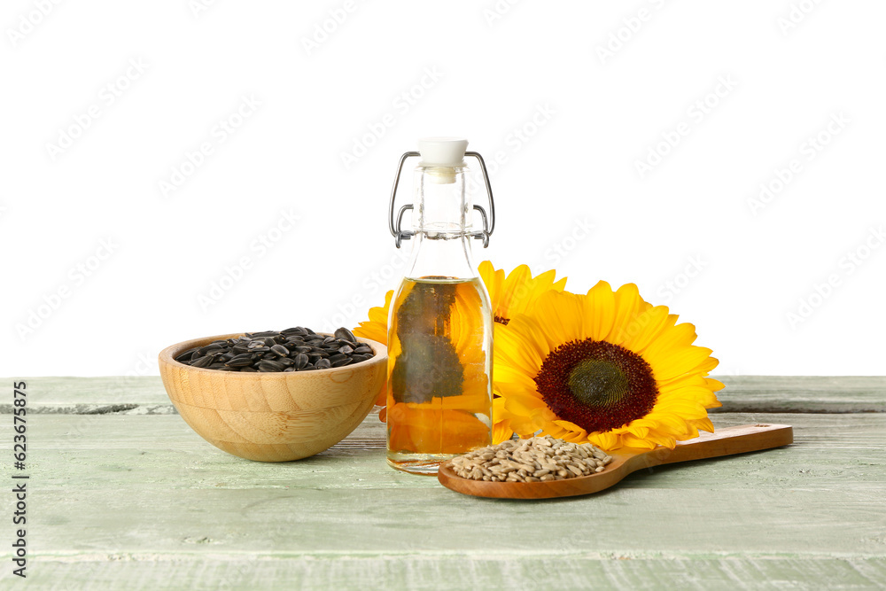 Sunflowers, seeds and bottle of oil on table against white background