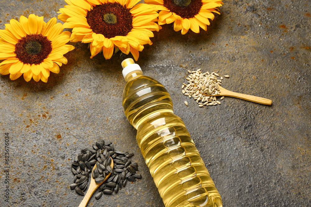 Sunflowers, seeds and bottle of oil on brown background