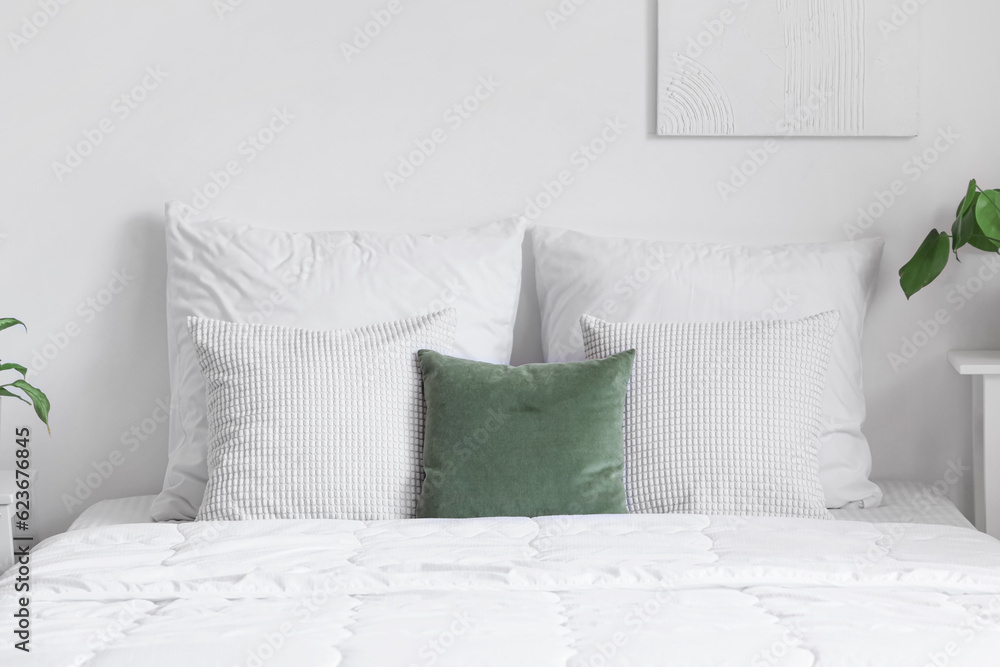 Cozy bed with white blanket and pillows in light bedroom