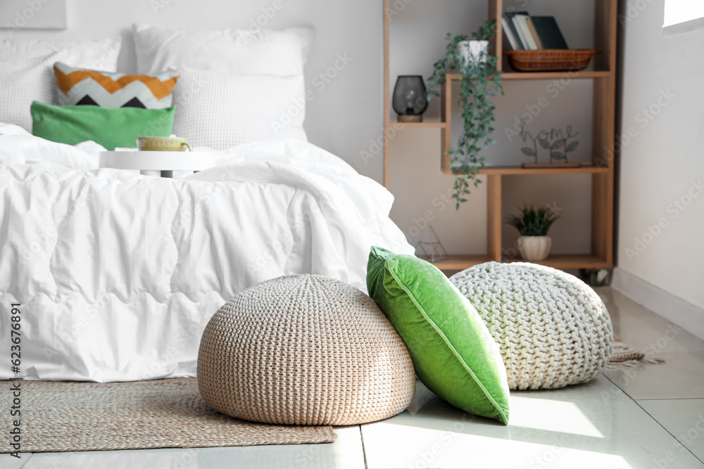 Cozy bed with white blanket and wicker pouf in interior of stylish bedroom