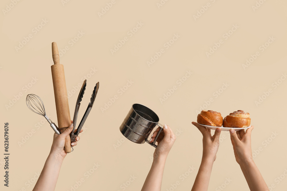 Female hands with baking utensils and cinnamon rolls on beige background