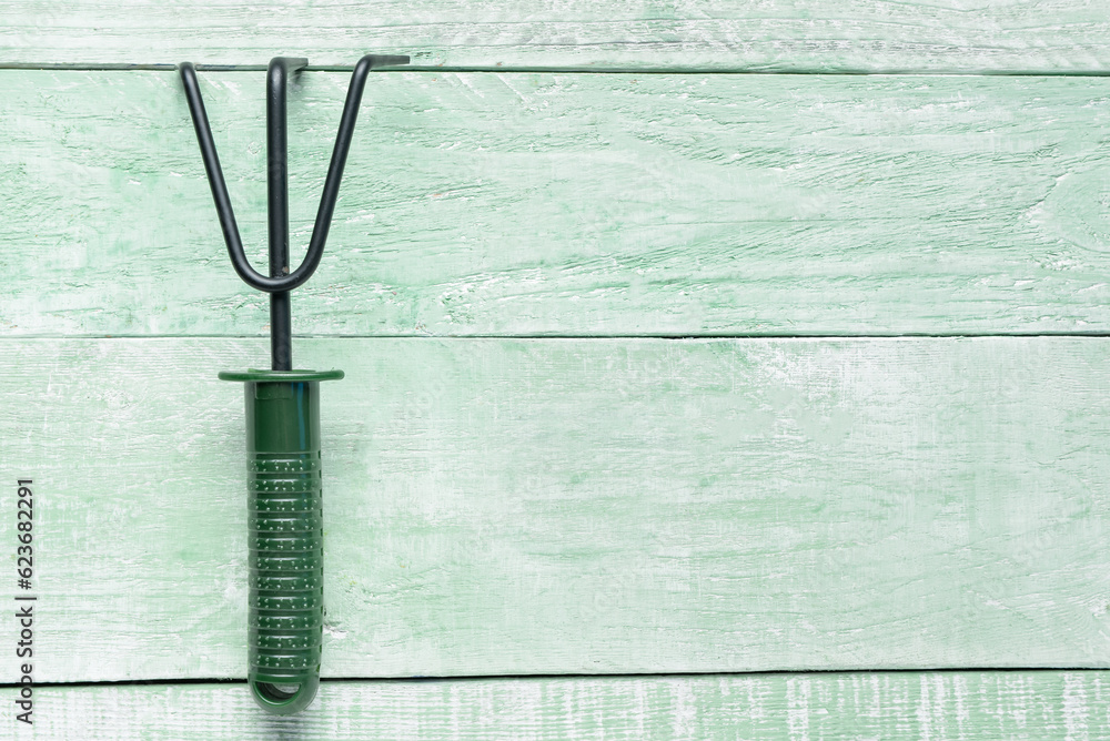 Gardening rake on green wooden background