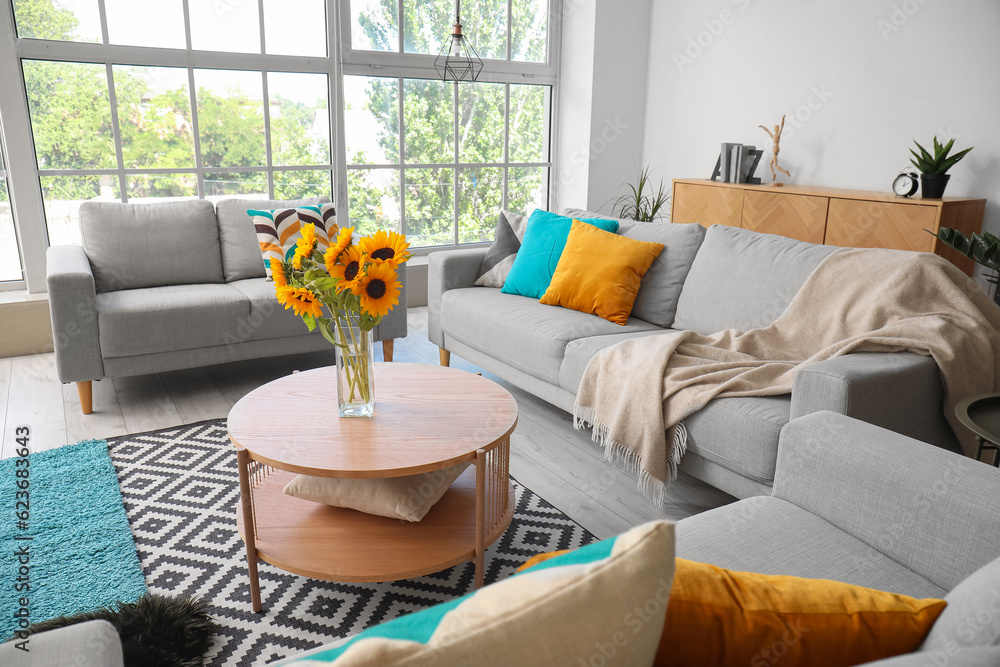 Cozy grey sofas and vase with beautiful sunflowers in interior of light living room