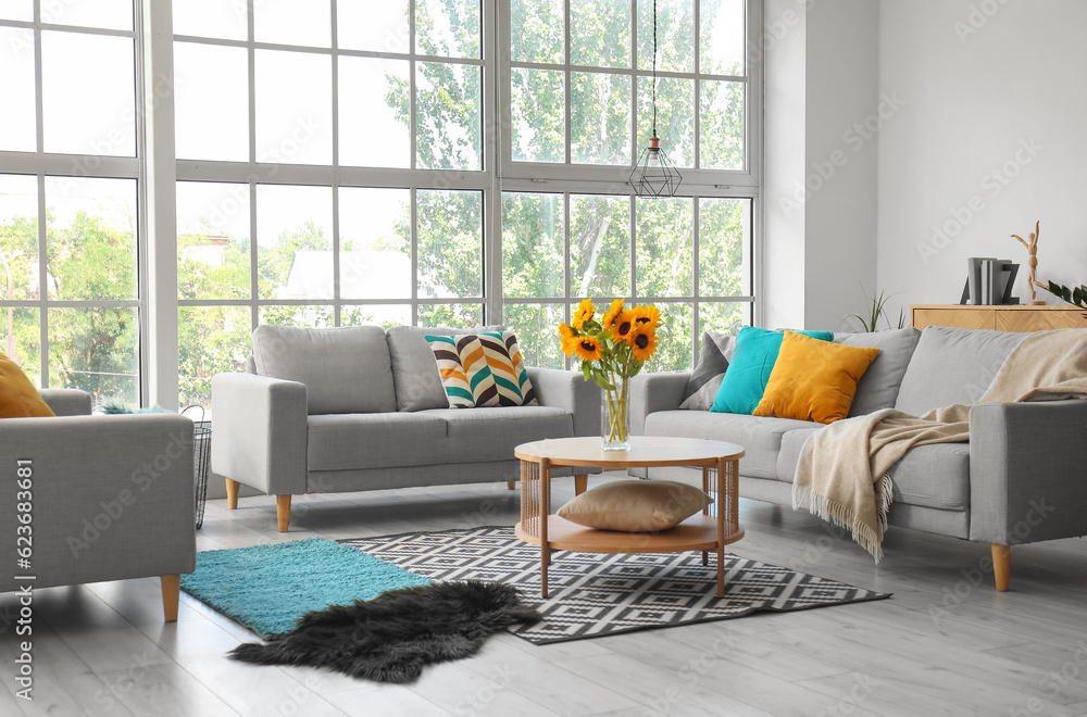 Cozy grey sofas and vase with beautiful sunflowers in interior of light living room