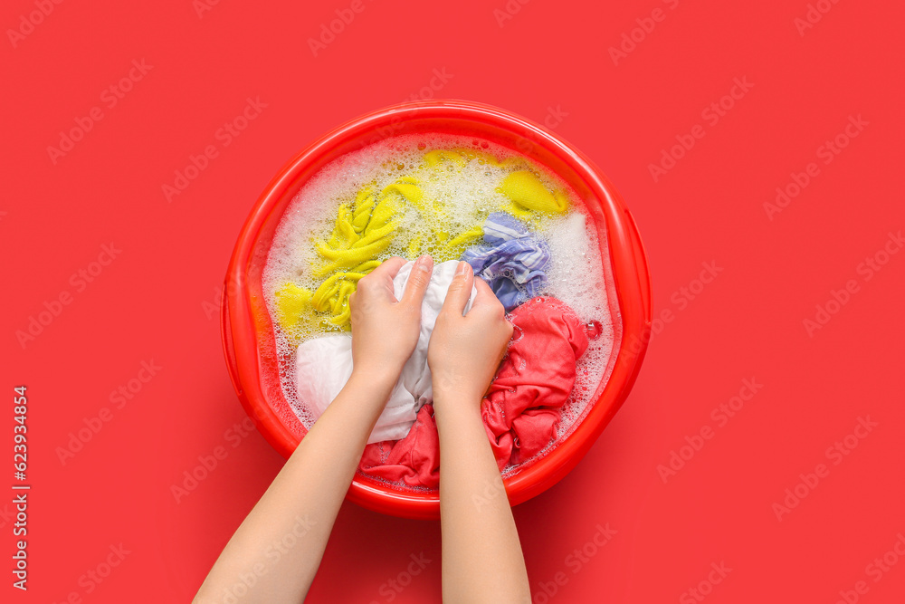 Woman washing laundry in plastic basin with water and foam on red background