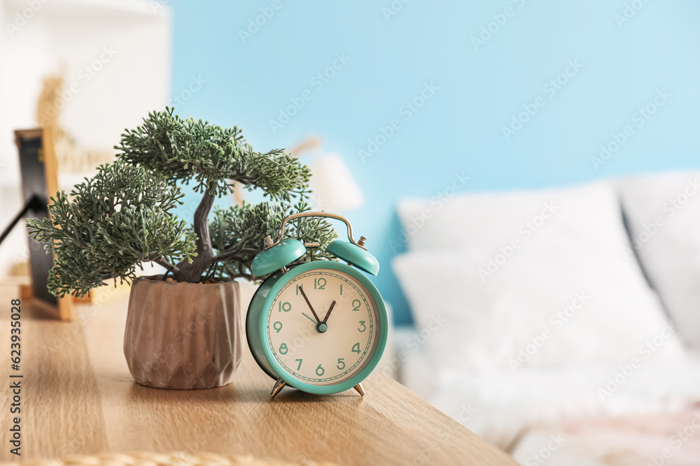 Vintage alarm clock with bonsai on table in bedroom, closeup